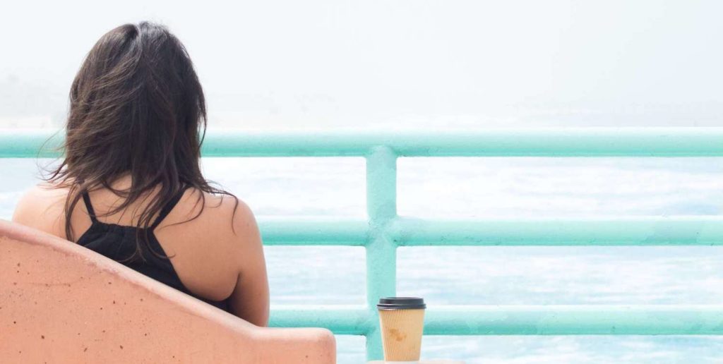 Woman sitting calming with coffee, staring at the ocean