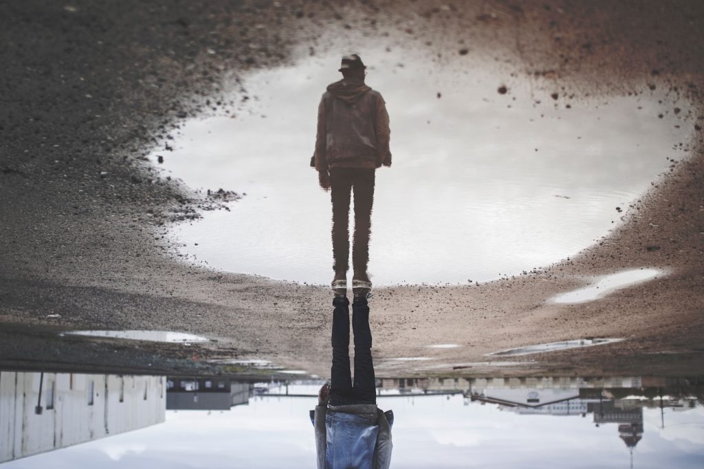 financial reality v fantasy - a man's reflection on a puddle, reversed so that his reflection appears to be standing upright