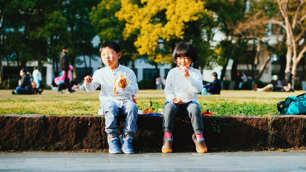 Guardar dinheiro na merenda escolar - um menino e uma menina se sentam lado a lado em uma parede de pedra, no mesmo parque, comer almoços