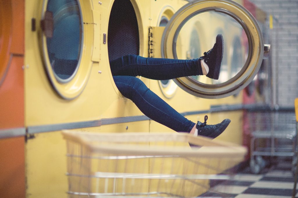 Woman's feet stick out of a yellow washing machine in a Laundromat - why messy bitches need a fuck up fund