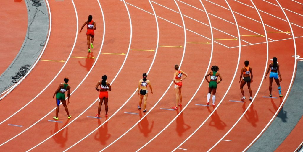 monthly savings - Seven women line up on a red running track, watching another woman running past