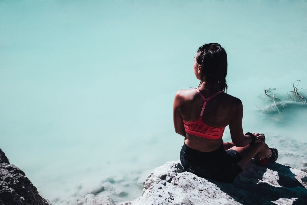A woman in a sports bra and shorts sits at the edge of a milky pond, staring across the water | Unhealthy goal setting