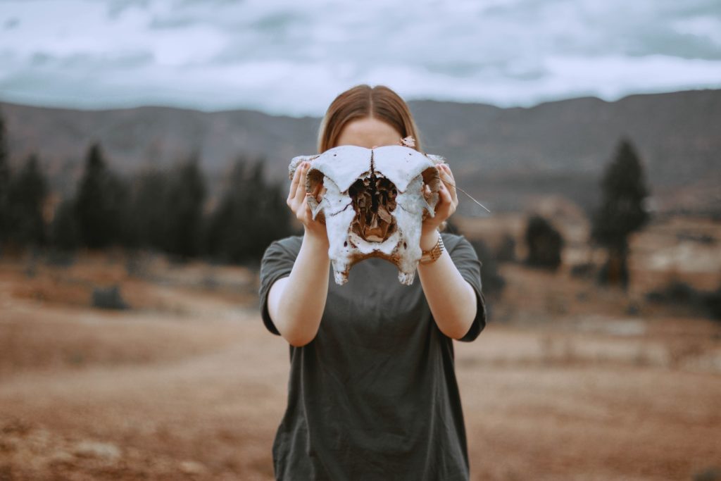 Internalized sexism and women's finances. A woman holds a bleached skull of a large animal in front of her face. She stands in front of a dessert landscape.