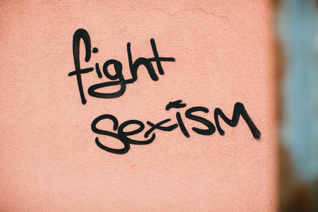 fight internalized sexism. The words "fight sexism" are spray painted in black on a light pink wall.